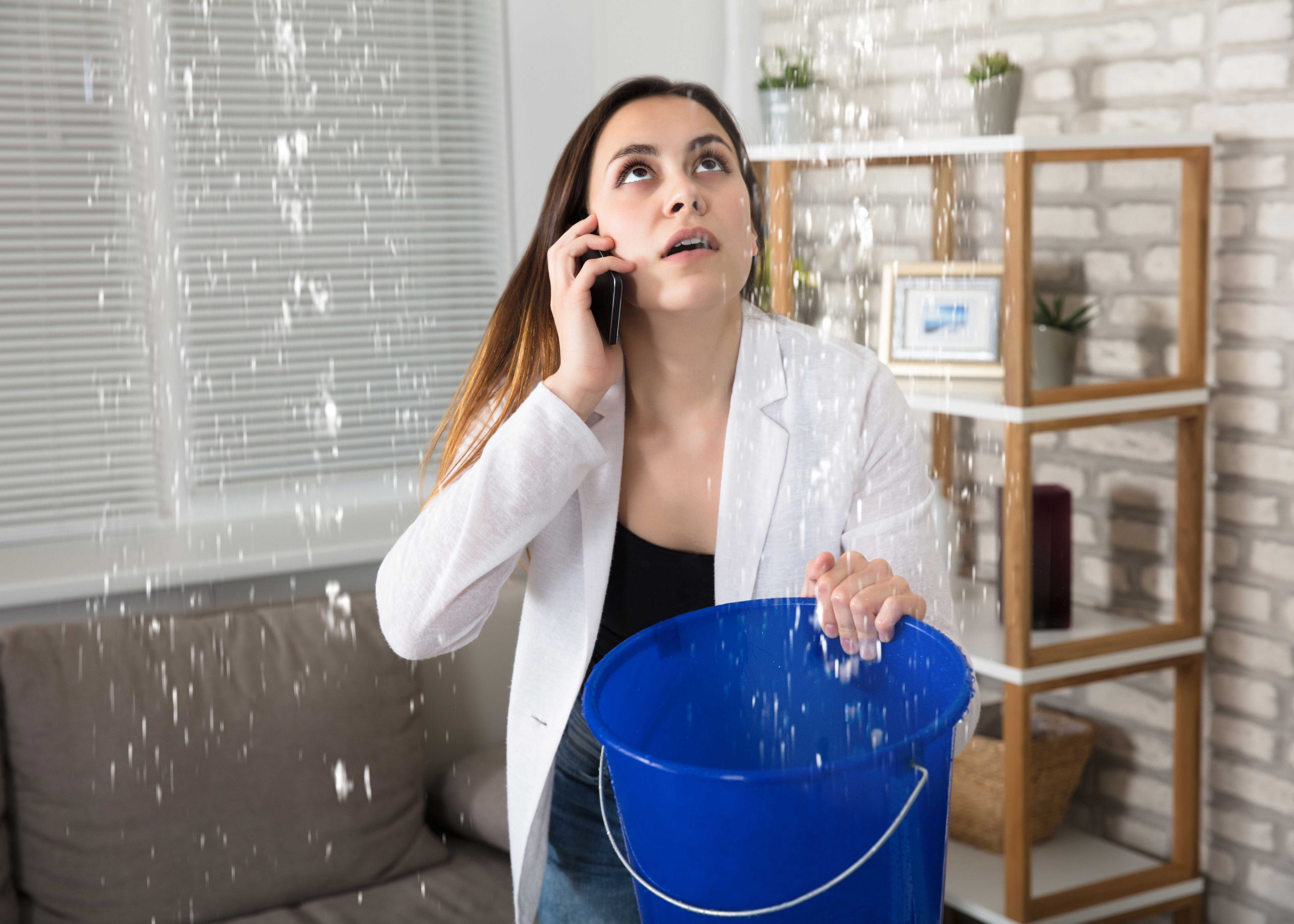 A woman in white and black holding a blue bucket handling water damage from leaking ceiling Flint, MI